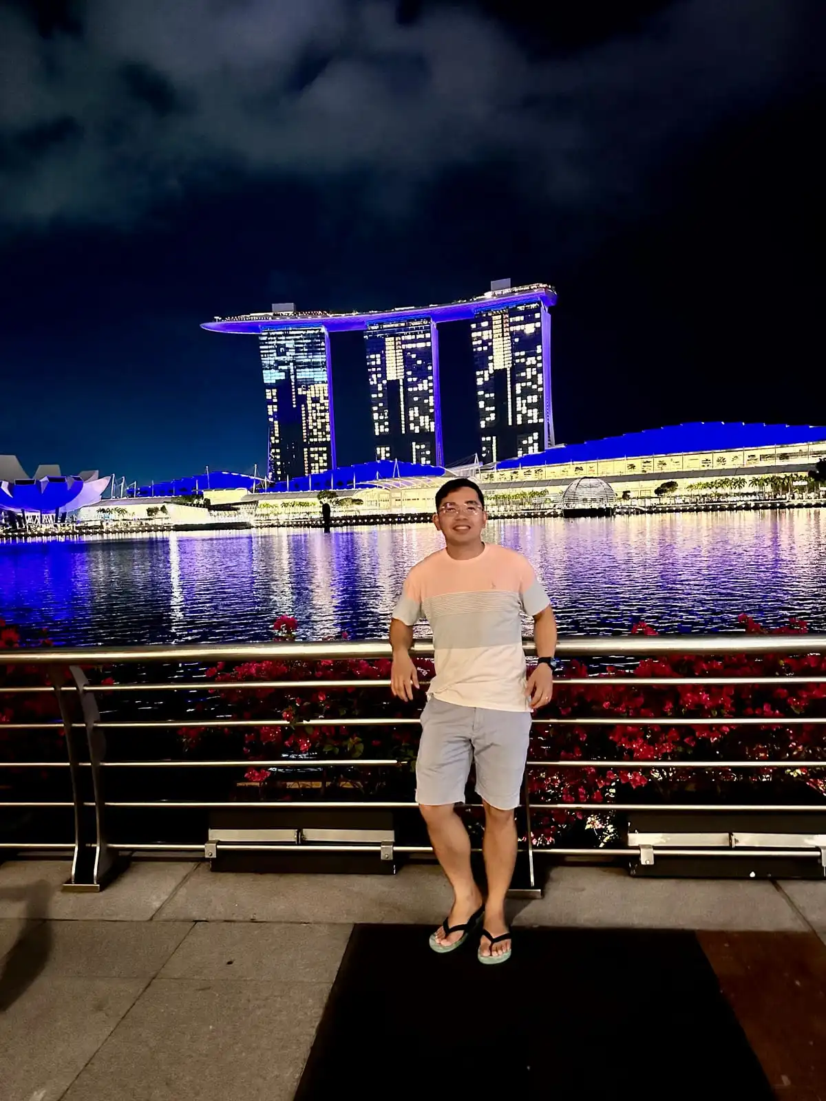 Standing along the waterfront at night with the Marina Bay Sands skyline lit up in blue behind