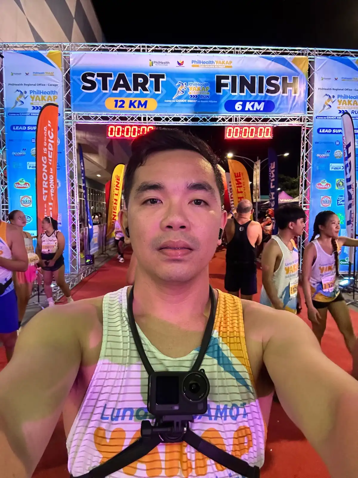 Selfie under the start and finish arch of a night fun run, with an action camera strapped to the chest